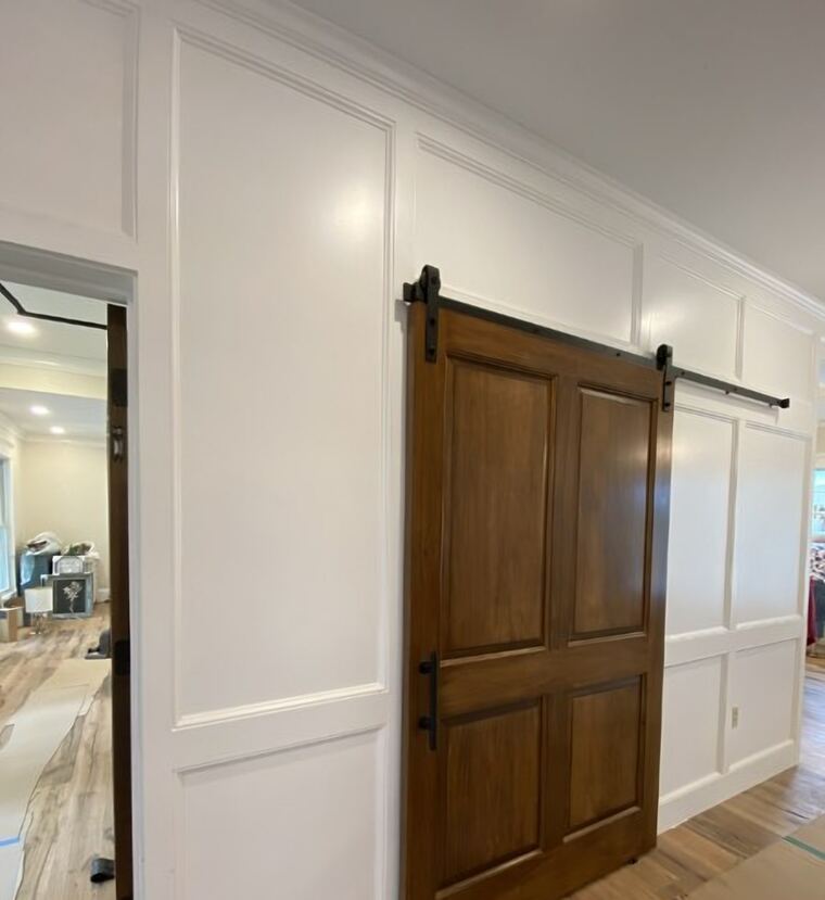 Sliding barn door in stained wood beside a panelled wall